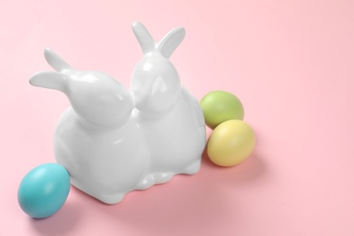 Photo of Ceramic Easter bunnies and dyed eggs on color background, space for text