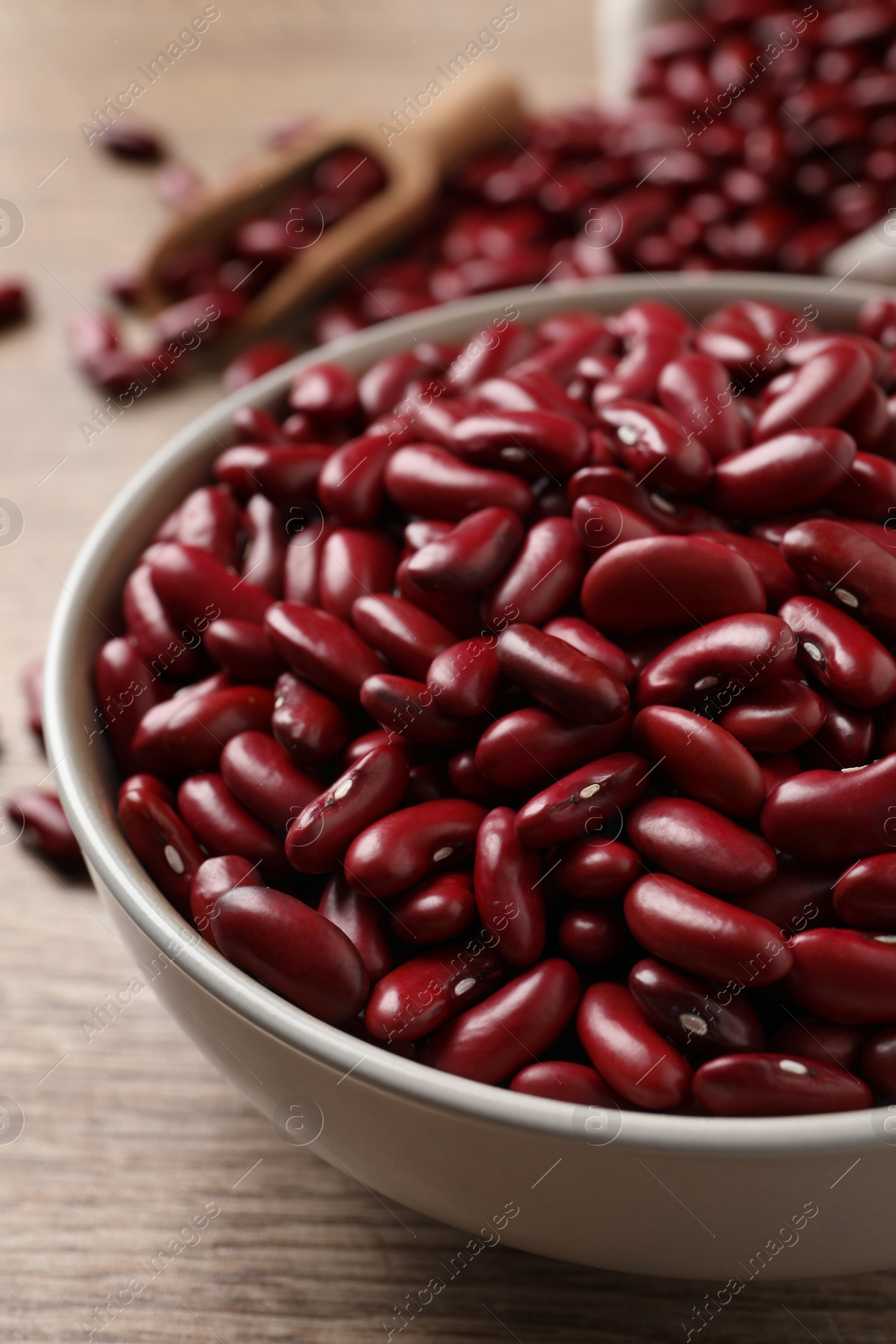 Photo of Raw red kidney beans in bowl on wooden table, closeup