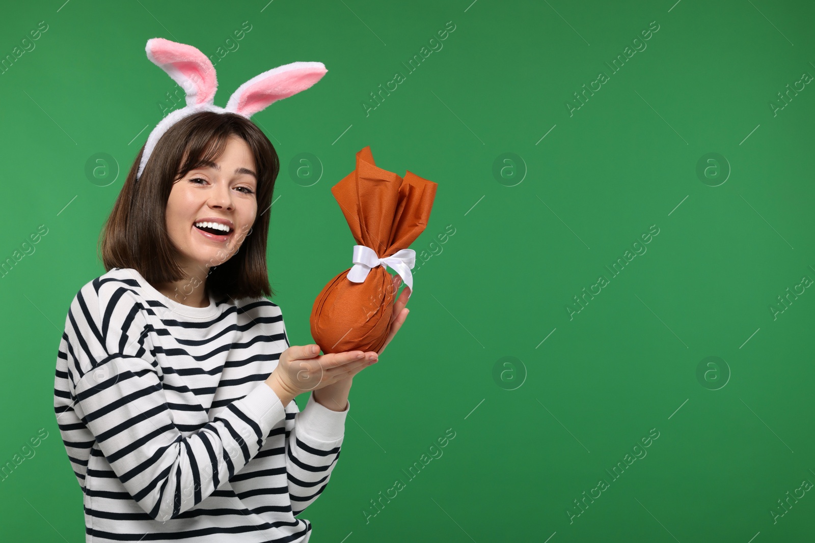 Photo of Easter celebration. Happy woman with bunny ears and wrapped egg on green background, space for text