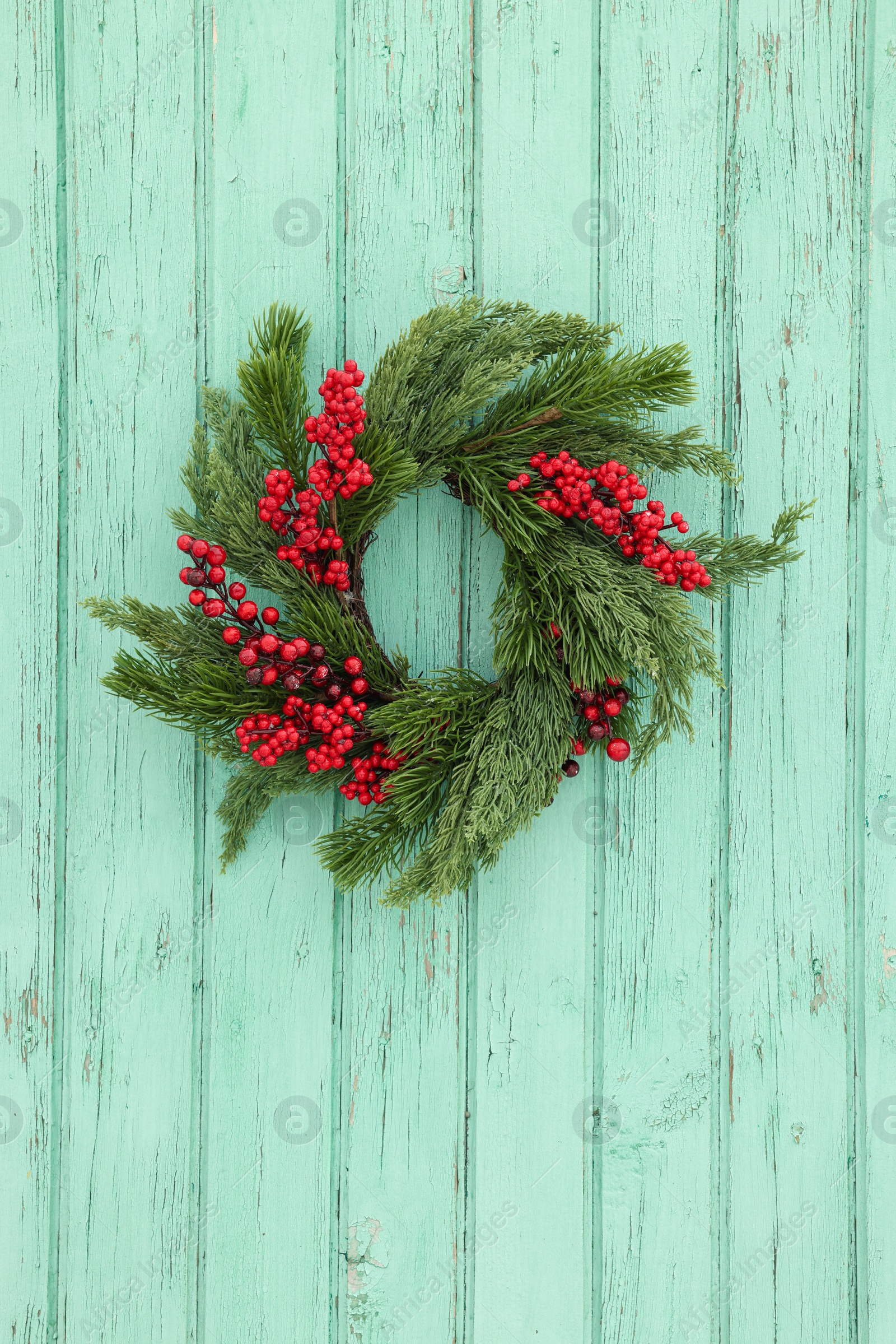 Photo of Beautiful Christmas wreath with red berries hanging on turquoise wooden wall