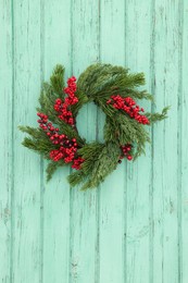 Beautiful Christmas wreath with red berries hanging on turquoise wooden wall