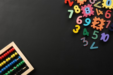 Photo of Many colorful numbers and mathematical symbols near abacus on black background, flat lay. Space for text