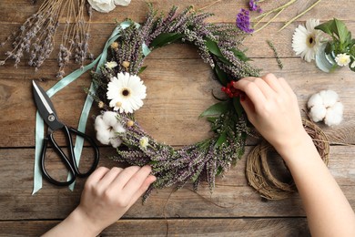 Photo of Florist making beautiful autumnal wreath with heather flowers at wooden table, top view