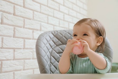 Cute little baby nibbling toy in high chair indoors. Space for text