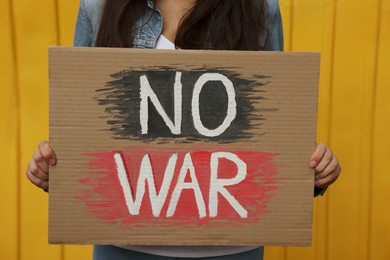 Photo of Woman holding poster No War near yellow fence, closeup