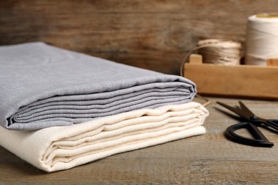 Photo of Folded hemp cloths and scissors on wooden table, closeup