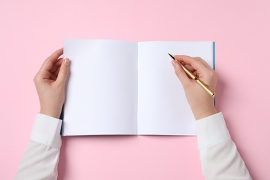 Photo of Woman with pen and notepad on pink background, top view