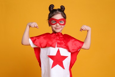 Cute little girl in superhero suit on yellow background