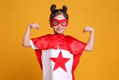 Photo of Cute little girl in superhero suit on yellow background