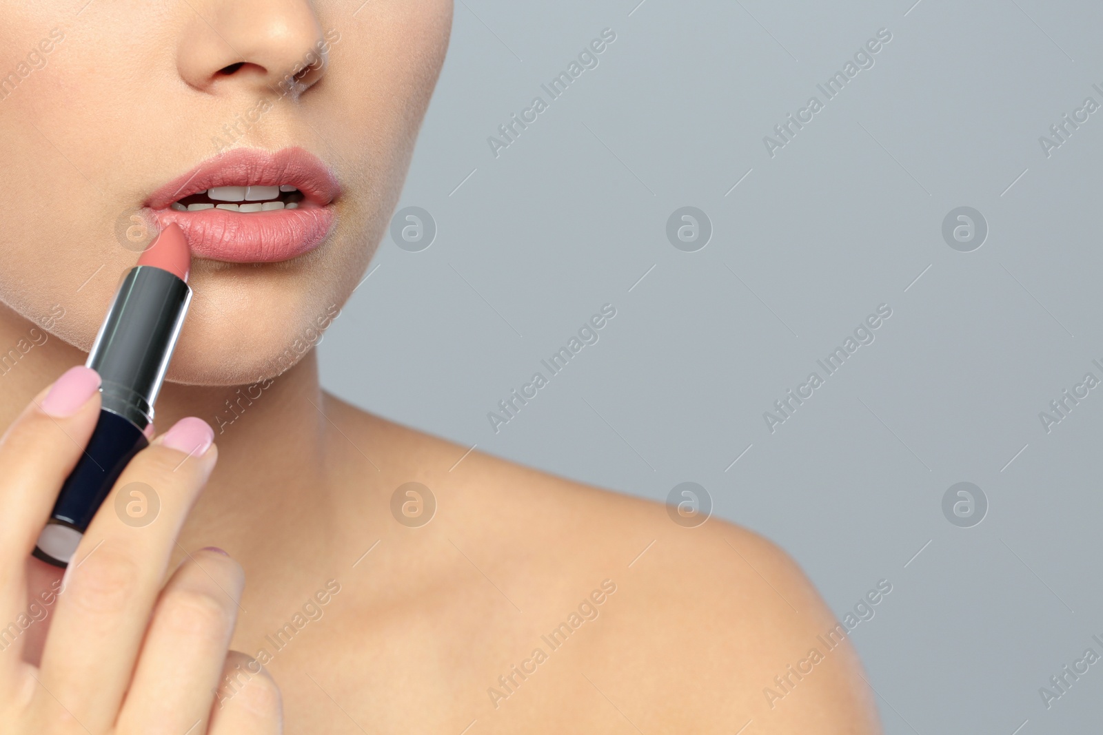 Photo of Young woman applying lipstick on color background, closeup. Space for text