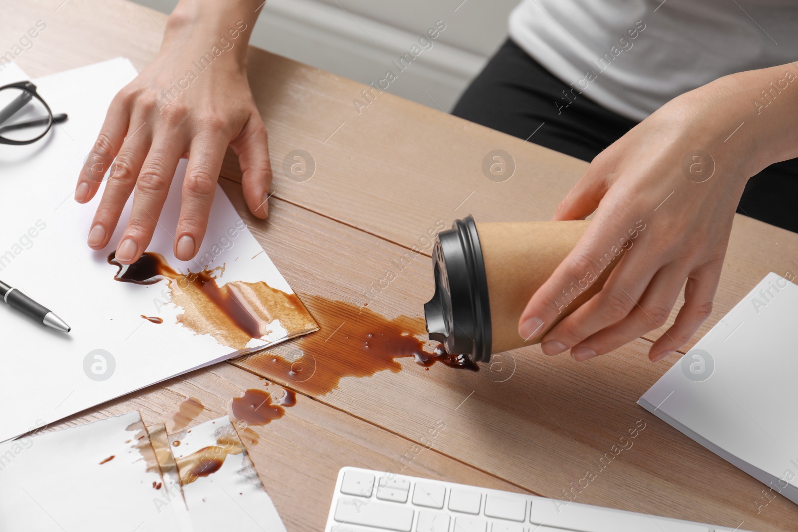 Photo of Woman spilled coffee on wooden office desk, closeup