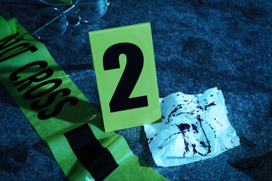 Photo of Bloody napkin, tape and crime scene marker on stone table at night