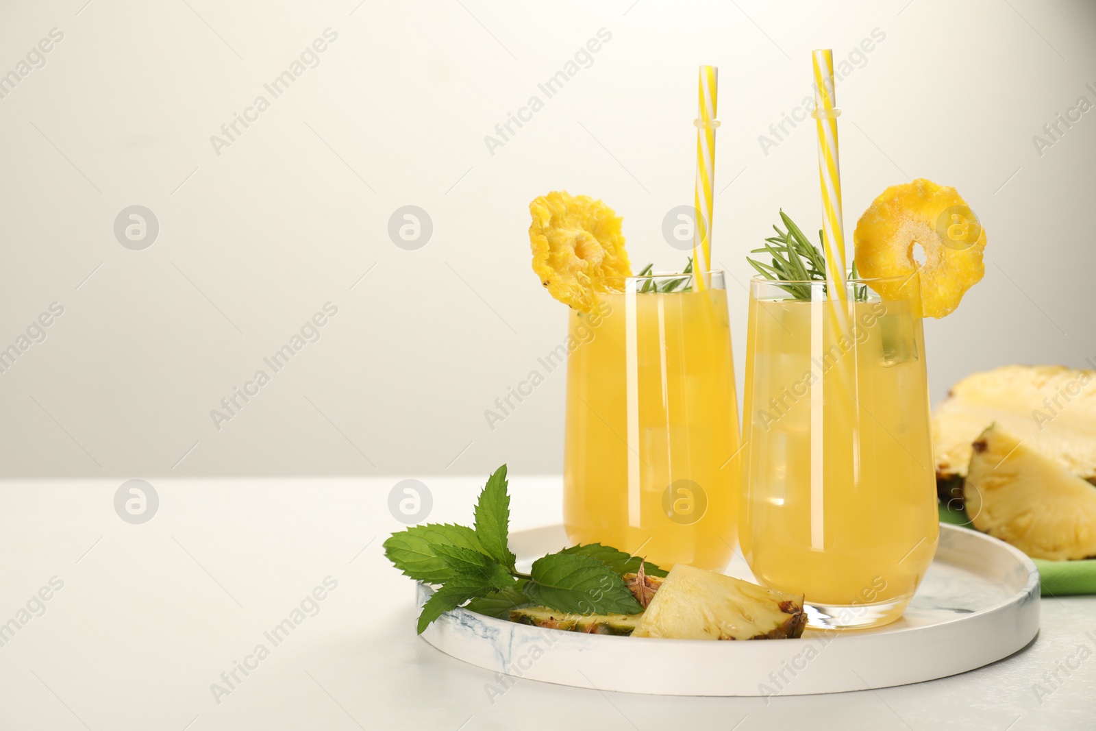 Photo of Glasses of tasty pineapple cocktail with rosemary, mint and sliced fruit on white table, space for text