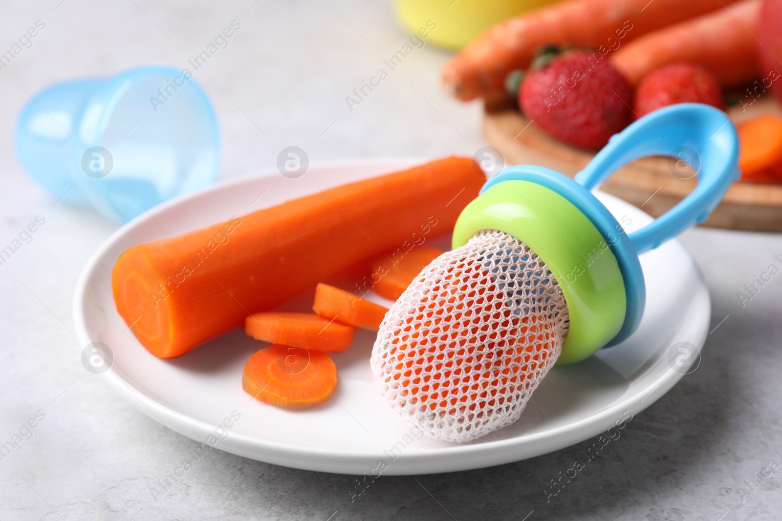 Photo of Nibbler with boiled carrot on light grey table, closeup. Baby feeder