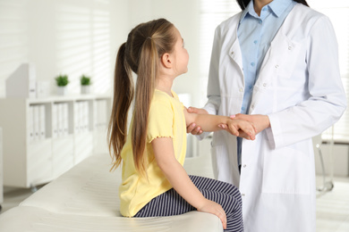 Professional orthopedist examining little patient's arm in clinic