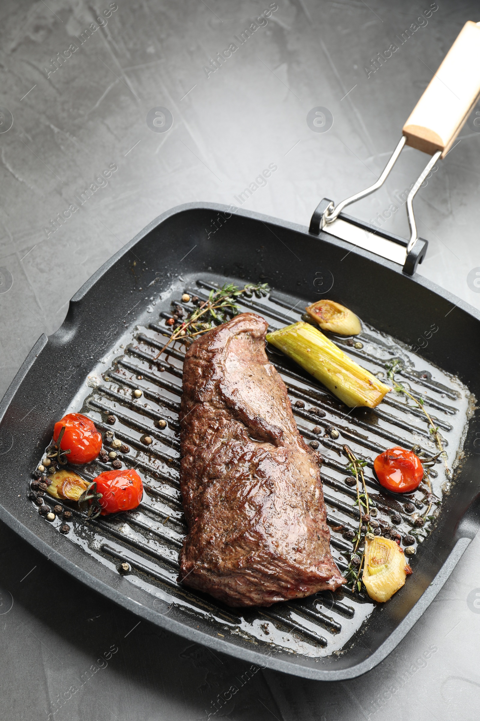 Photo of Delicious grilled beef meat and vegetables in pan on grey table, closeup