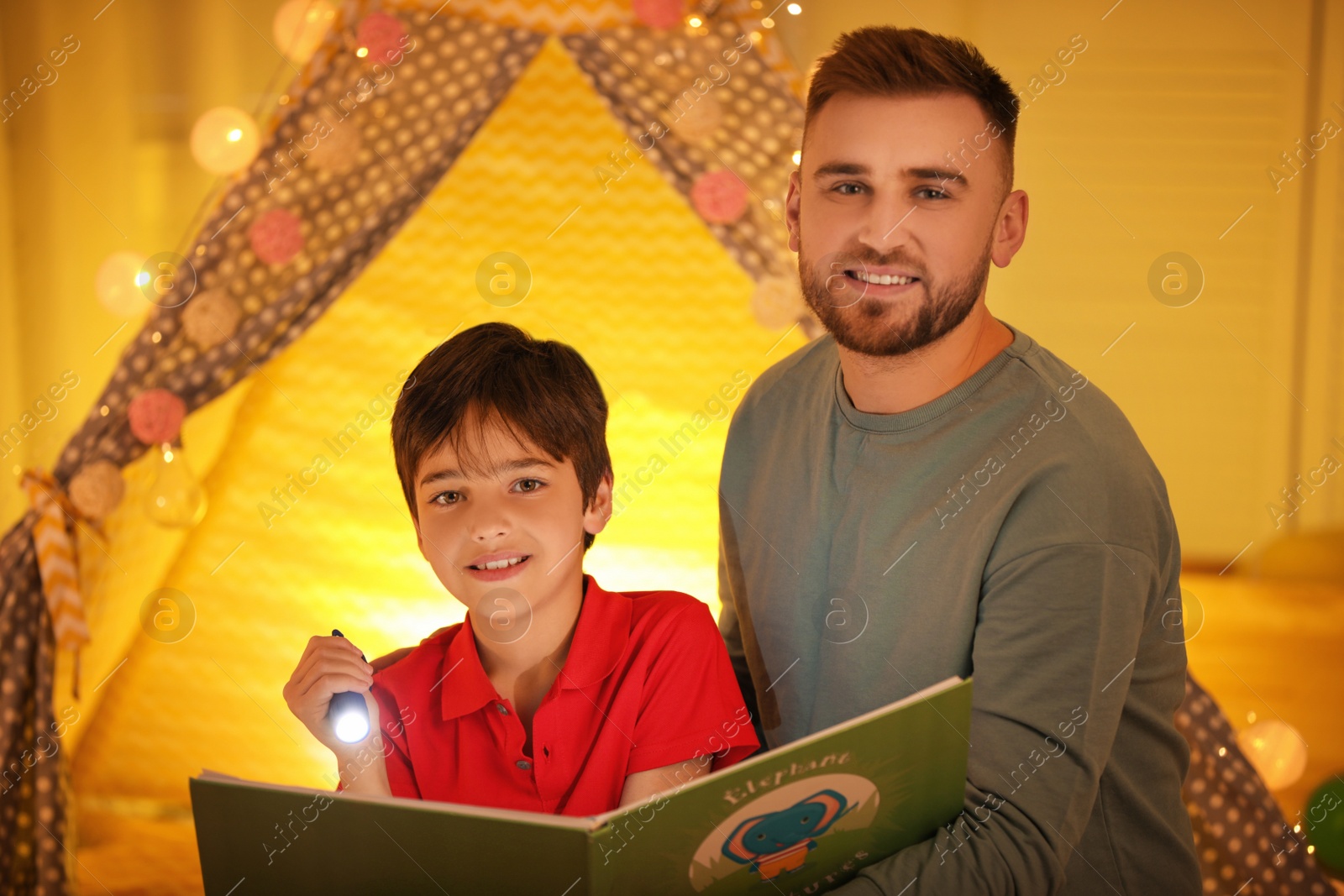 Photo of Father and son with flashlight reading book at home