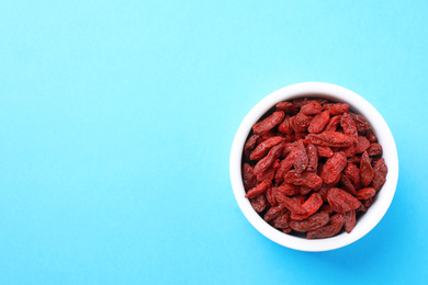 Photo of Dried goji berries in bowl on light blue background, top view. Space for text