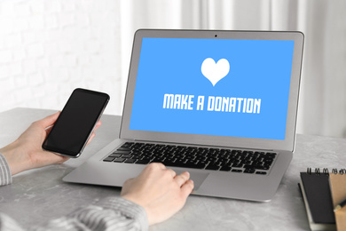 Image of Donations concept. Woman with smartphone working on laptop at table, closeup