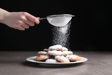 Woman with sieve sprinkling powdered sugar onto cookies at grey textured table, closeup