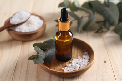 Photo of Aromatherapy. Bottle of essential oil, sea salt and eucalyptus leaves on wooden table