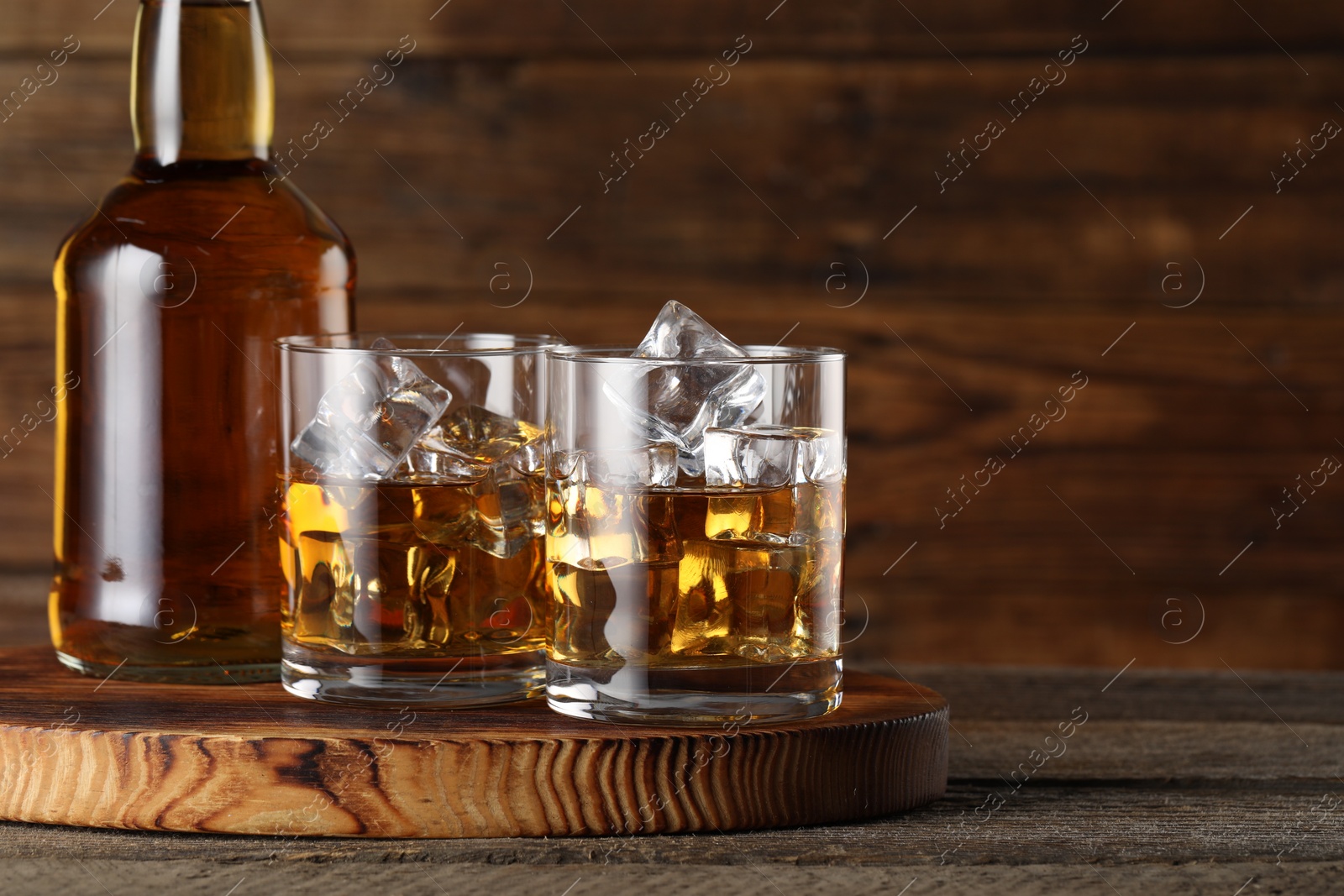 Photo of Whiskey with ice cubes in glasses and bottle on wooden table, closeup. Space for text