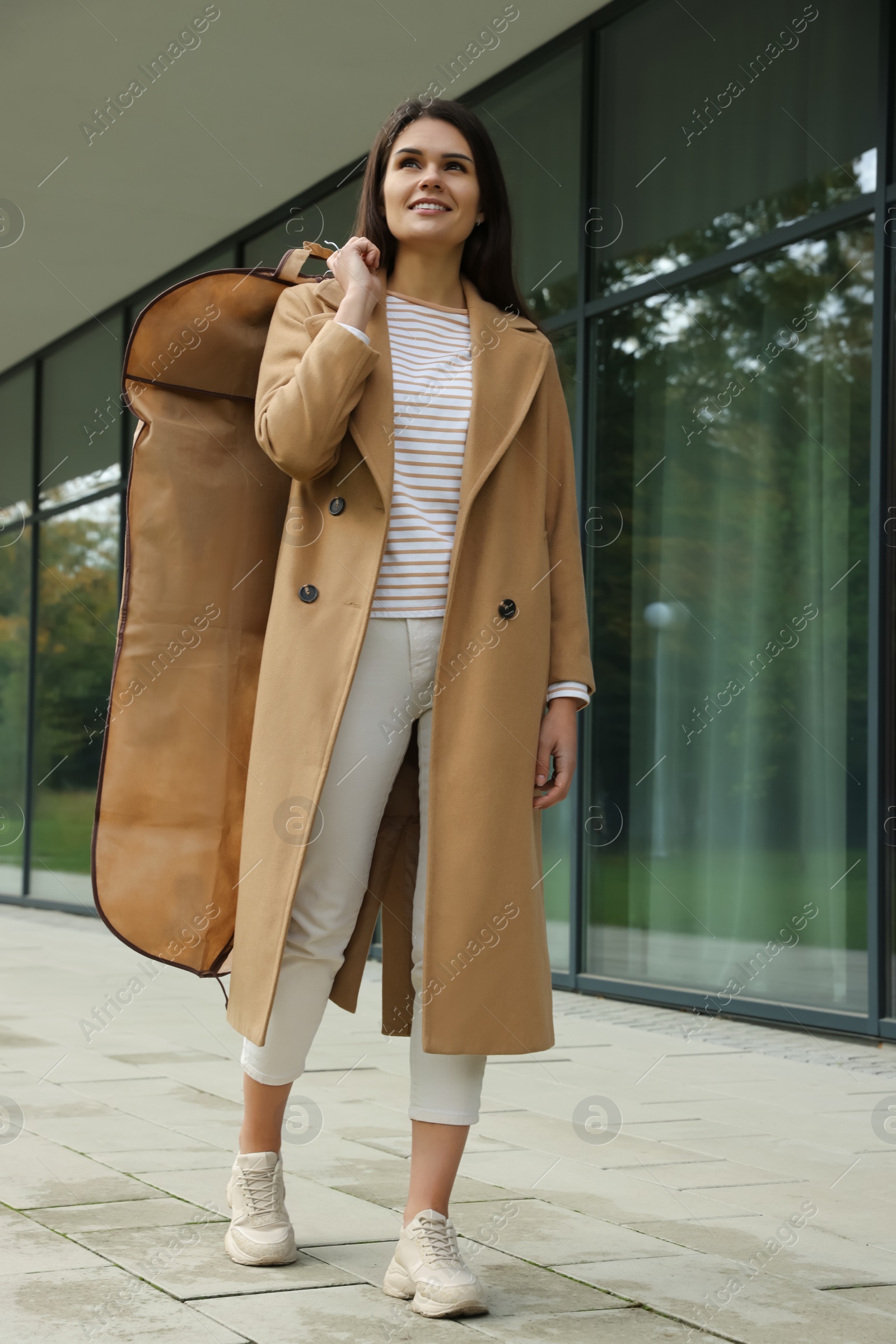 Photo of Attractive happy woman holding garment cover with clothes outdoors. Dry cleaning service