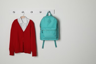 Photo of Shirt, jumper and bag hanging on white wall. School uniform. Space for text