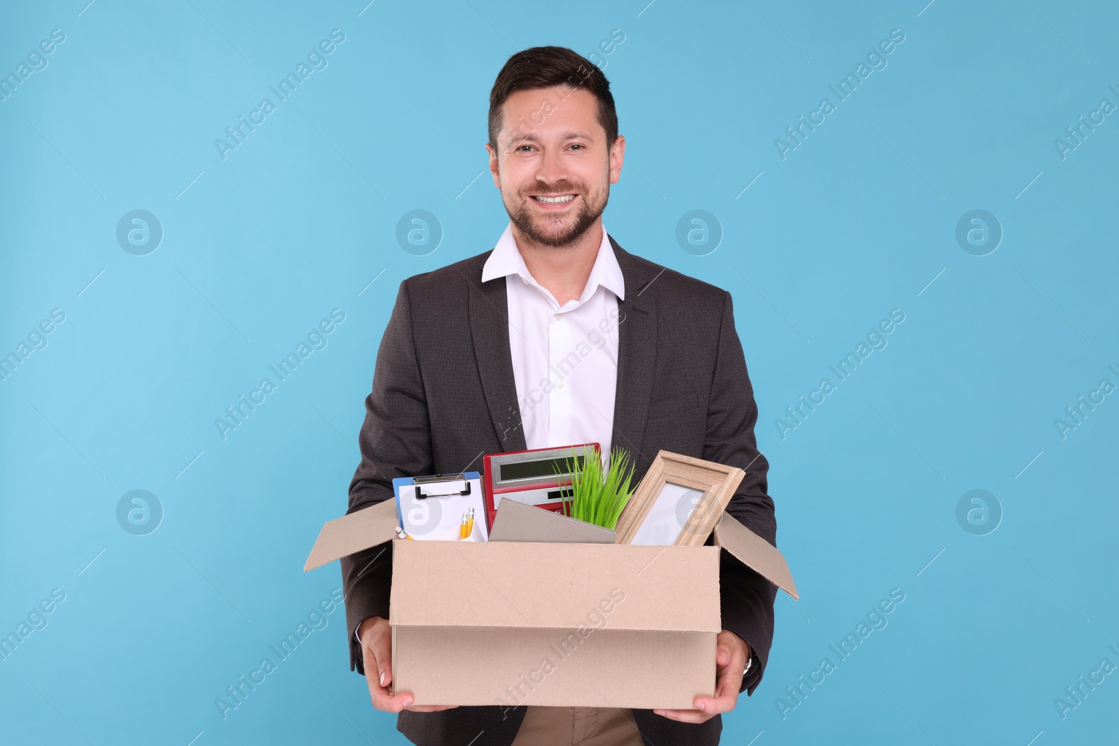 Photo of Happy unemployed man with box of personal office belongings on light blue background