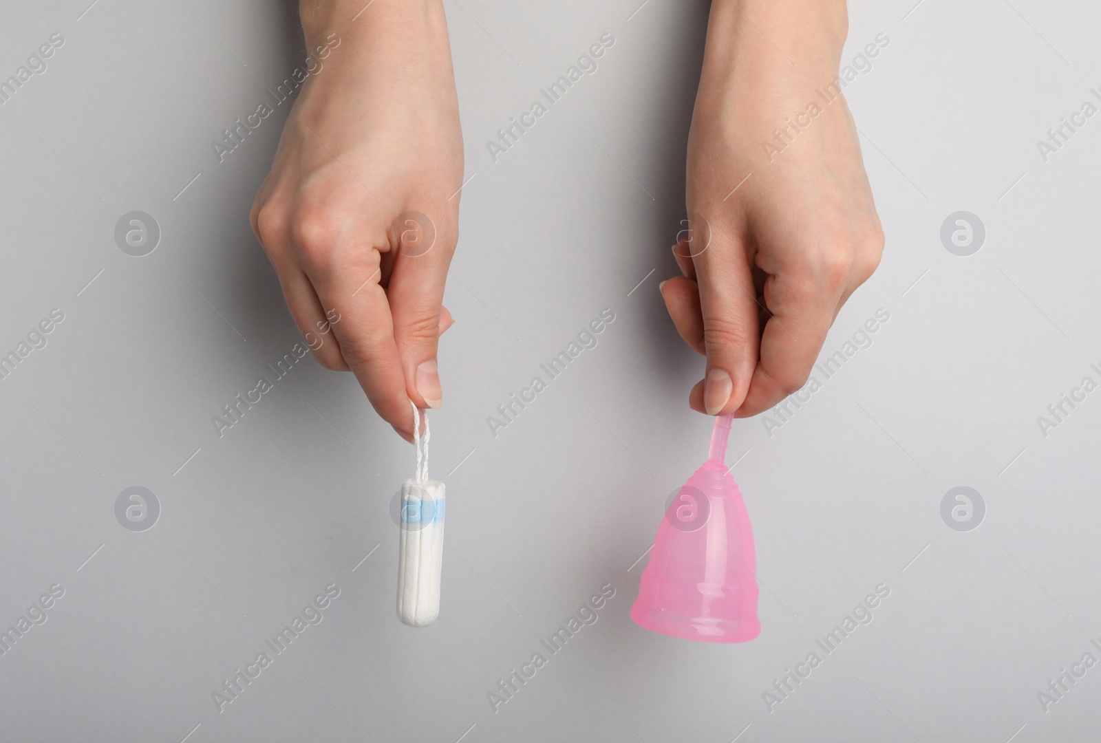 Photo of Woman holding menstrual cup and tampon on grey background, top view