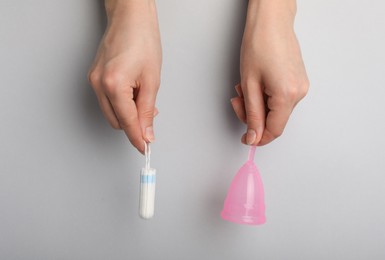 Woman holding menstrual cup and tampon on grey background, top view
