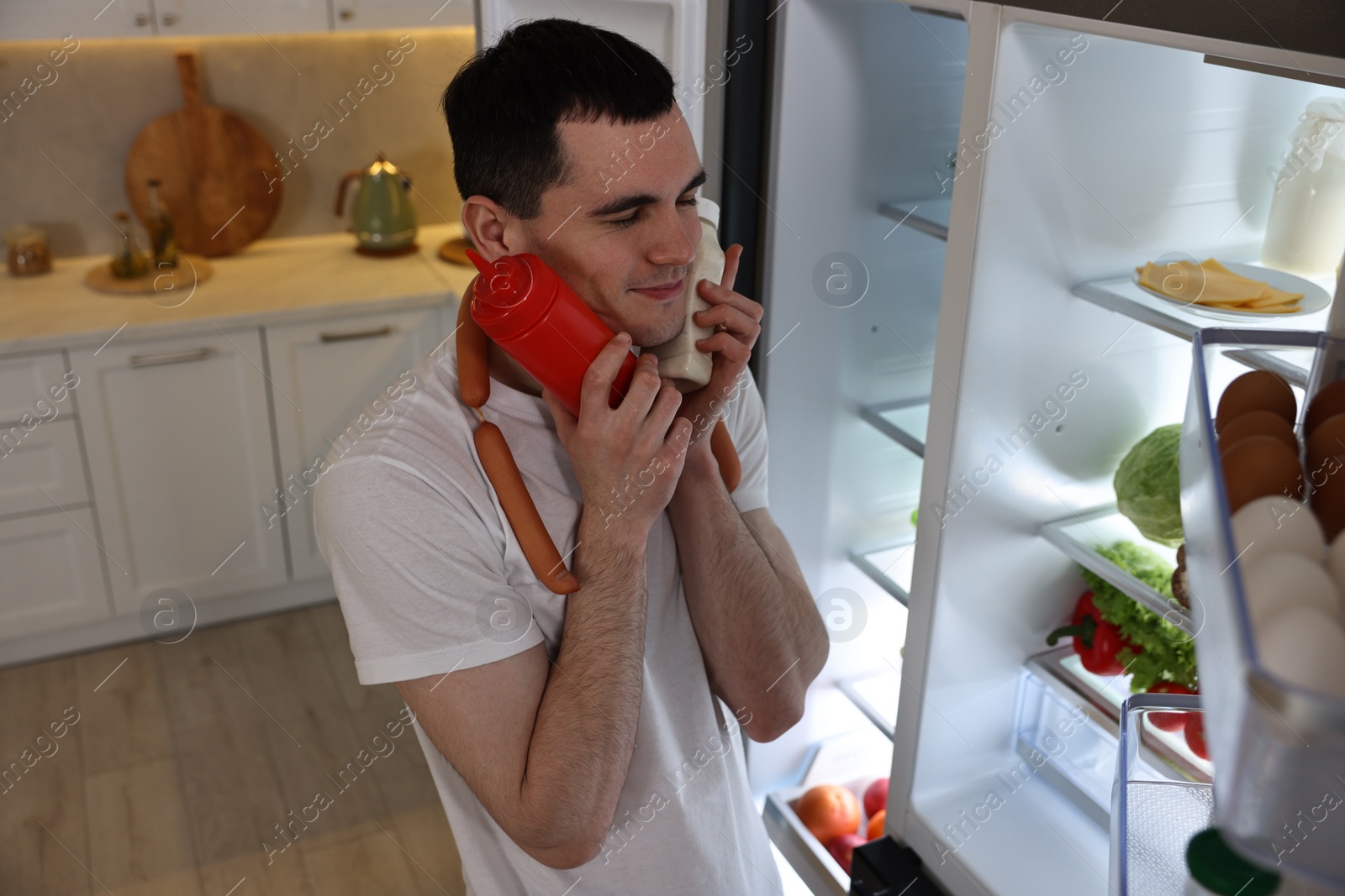 Photo of Man with sauces and sausages near refrigerator in kitchen