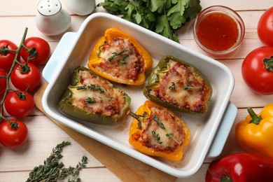 Photo of Tasty stuffed peppers in dish and ingredients on wooden table, flat lay