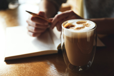 Woman with notebook and cup of latte at wooden table, closeup