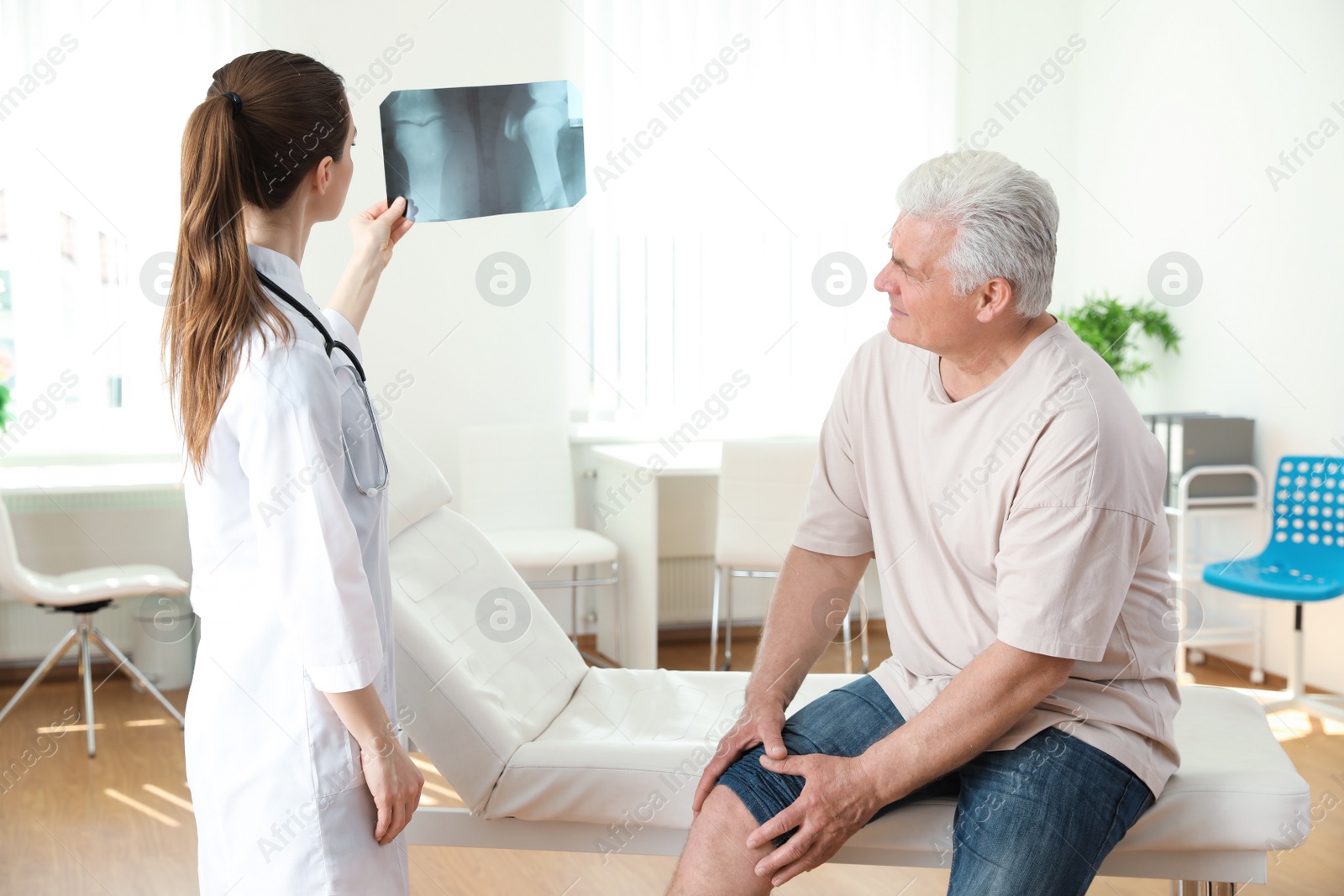 Photo of Young doctor with X-ray and senior patient in clinic. Knee problem