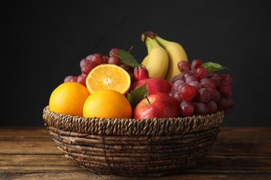 Wicker basket with different fruits on wooden table, closeup