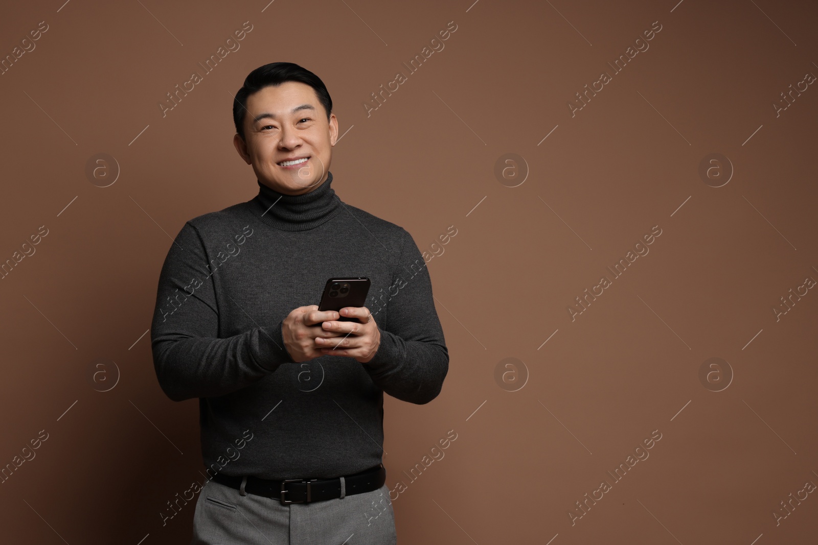 Photo of Portrait of happy man with smartphone on brown background. Space for text