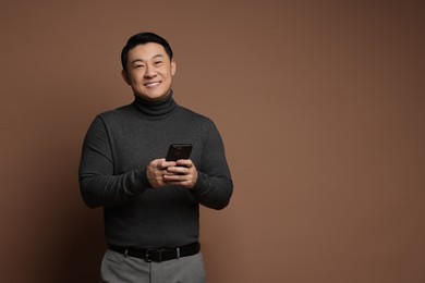 Photo of Portrait of happy man with smartphone on brown background. Space for text