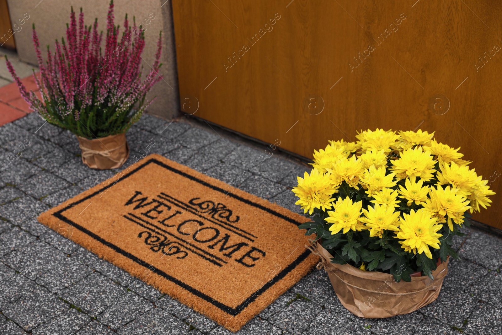 Photo of Doormat with word Welcome and beautiful flowers on floor near entrance