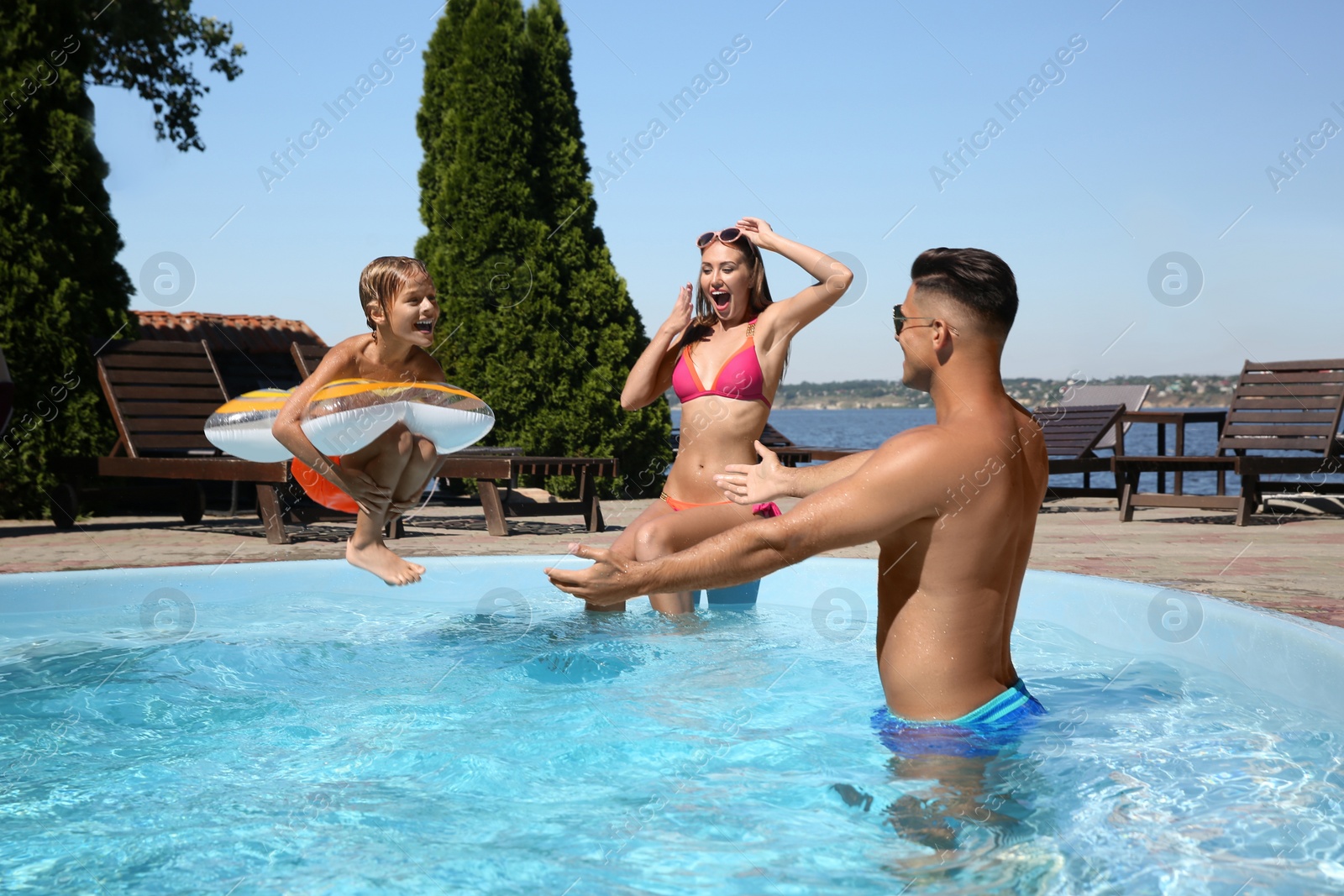 Photo of Happy family spending time in outdoor swimming pool on sunny summer day