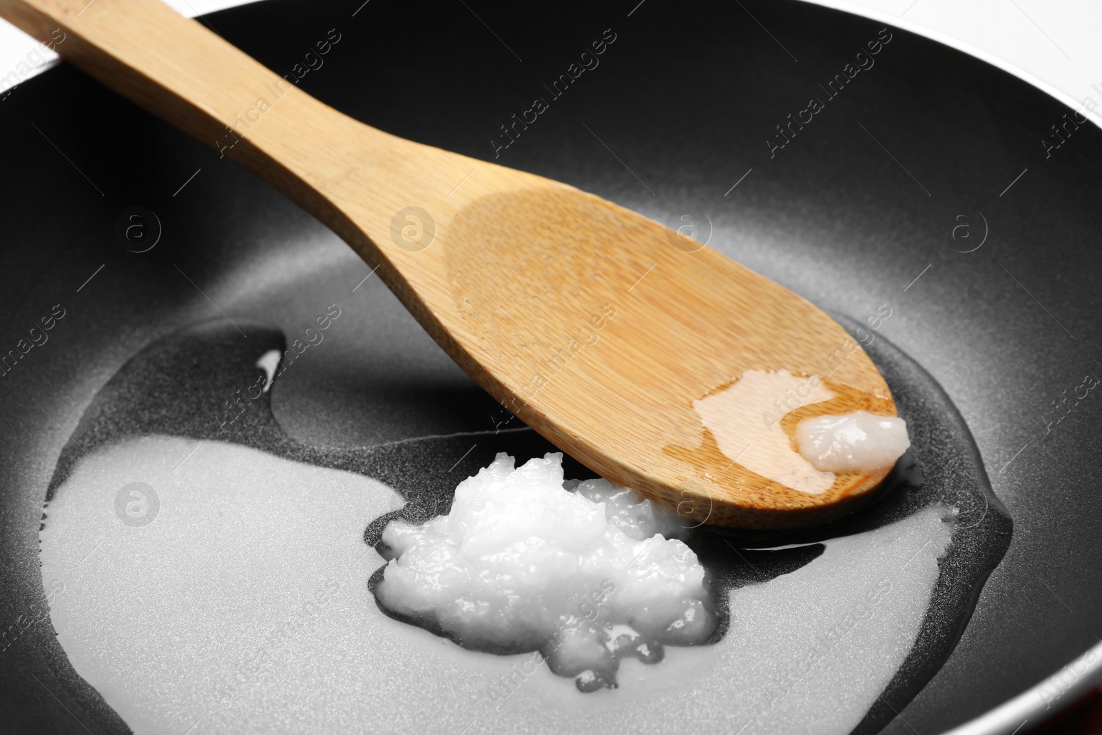 Photo of Frying pan with coconut oil and wooden spoon, closeup. Healthy cooking