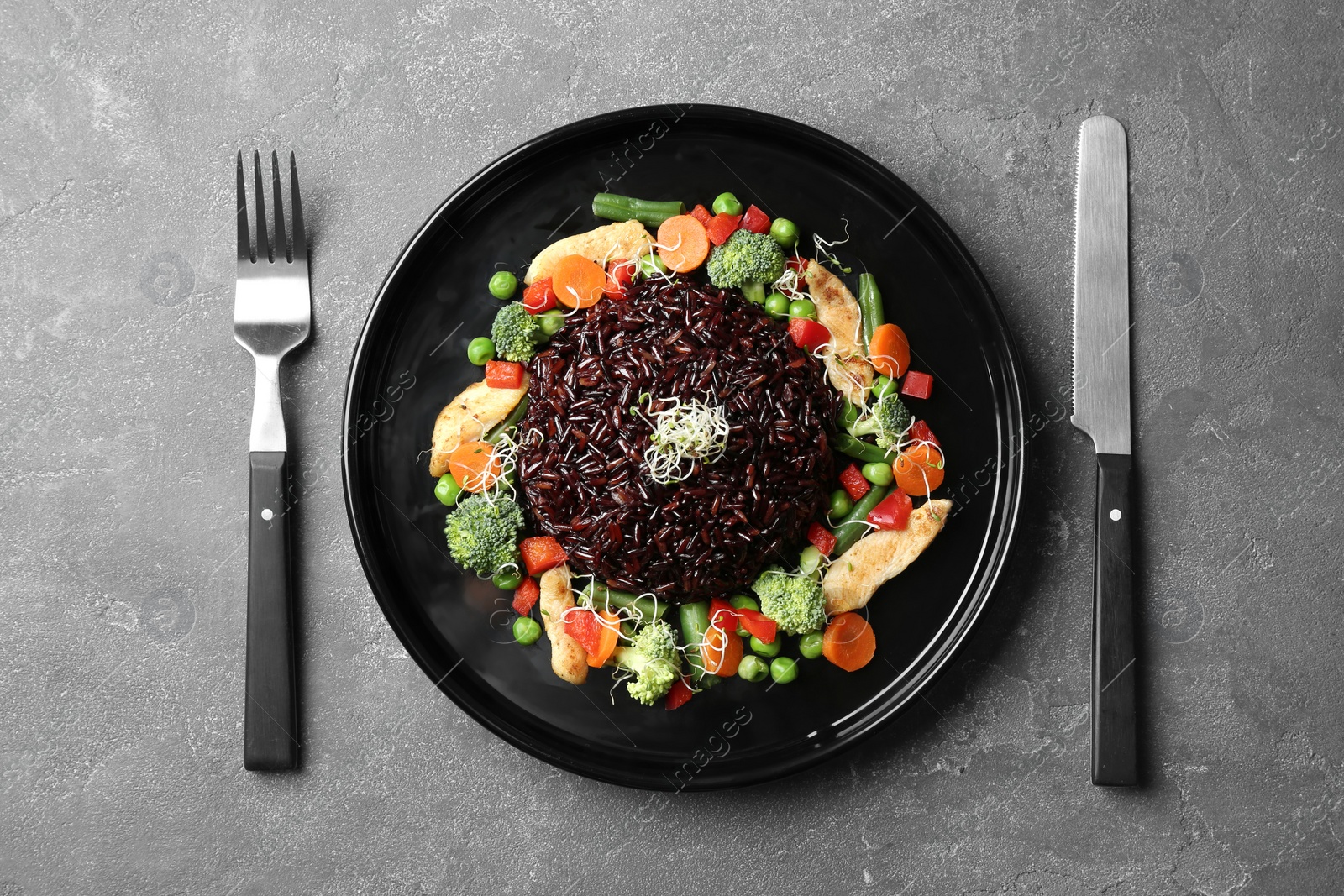 Photo of Plate of cooked brown rice and cutlery on table, top view