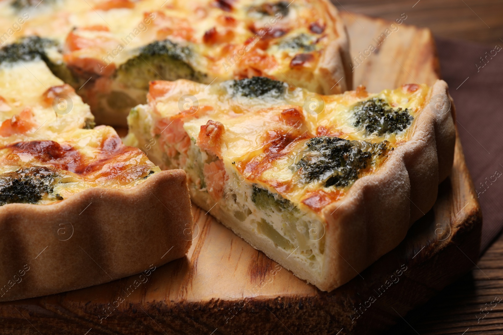 Photo of Delicious homemade quiche with salmon and broccoli on wooden board, closeup
