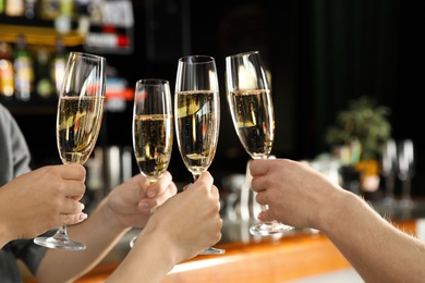 Photo of Friends clinking with glasses of champagne in bar, closeup