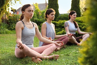 Photo of Young women meditating on green grass outdoors. Morning yoga
