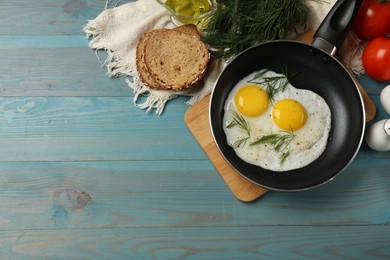 Photo of Frying pan with tasty cooked eggs, dill and other products on light blue wooden table, flat lay. Space for text