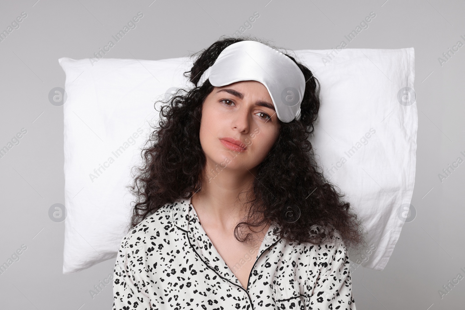 Photo of Tired young woman with sleep mask and pillow on light grey background. Insomnia problem