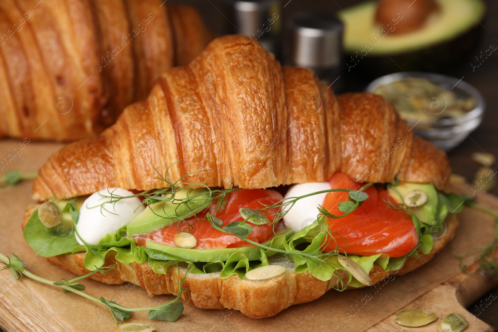 Photo of Tasty croissant with salmon, avocado, mozzarella and lettuce on table, closeup