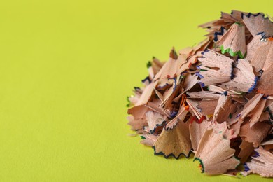 Pile of colorful pencil shavings on light green background, closeup. Space for text