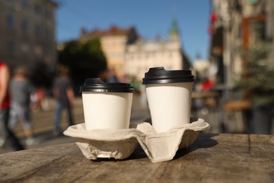 Photo of Cardboard takeaway coffee cups with plastic lids and holder on wooden table in city
